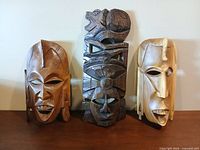 Front view of all three carved wood masks standing side by side