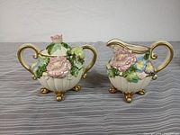 front view of sugar bowl and creamer showing floral relief and gold accents