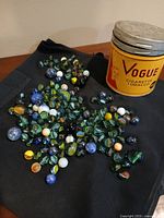 Tin and spread of assorted marbles on cloth background
