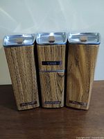 Front view of three stacked/adjacent canisters showing labels sugar, tea/coffee, flour, teak handled lids