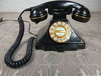 Front view of black rotary-style push-button telephone with handset on cradle and coiled cord visible