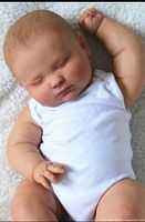 Full view of sleeping reborn baby doll in white onesie, lying on blanket