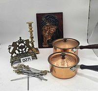Group shot of all items: two copper saucepans, brass menorah, brass candlestick, copper relief plaque, bundle of metal skewers