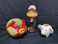 Group shot of all three banks: red hand-painted pig, poker pennies jar, white Stangl pig