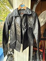 Front view of black leather jacket on hanger showing zipper, collar, sleeves