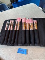 Open roll-up case with eight new makeup brushes showing pink bristles, gold ferrules, black handles, plastic tip covers