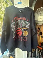 Full view of black Toronto Raptors graphic sweatshirt hanging