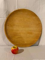 Front view of round blond wood platter with apple for scale