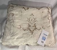 Folded cream linen tablecloth showing scalloped edge, embroidery and cutwork