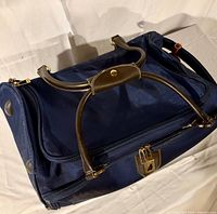 Top view showing navy fabric, brown handles, zippered opening, logo plate