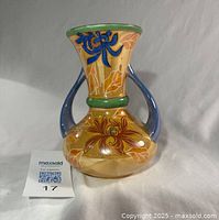 Front view of orange ceramic vase with blue handles and floral design