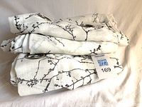 Three folded curtain panels showing grommets and pattern with lot tag visible