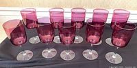 All ten cranberry glass wine glasses lined up showing color and clear stems