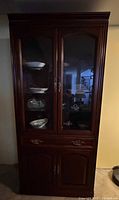 Full view of tall dark wood display cabinet with glass upper doors and lower storage doors