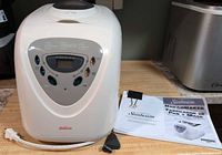 Breadmaker front view with manual, blade and power cord visible