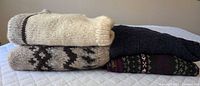 Stack of four folded sweaters showing colours and knit patterns