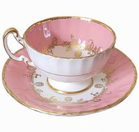 Teacup on saucer showing exterior pink glaze, gold trim, fluted form