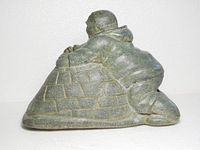Left profile of soapstone sculpture showing Inuit figure leaning on partially built igloo