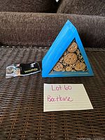 Front view of triangular blue bee house with bamboo tubes and wood discs, tag visible