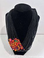 Full view of necklace on display bust showing multi-strand black beads and multicoloured accent cluster