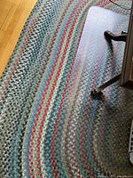 Clear plastic chair mat lying on multicolour braided rug, showing overall size and transparency