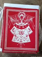 Stack of red cards showing front angel design with "Gloria" banner and envelopes behind