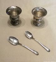 Two sterling toothpick holders and two spoons on neutral background