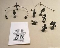Group view of seven brass figures, two wire balancing pieces, and book