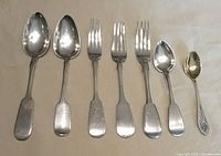 All seven pieces laid out side by side: four large spoons, three forks, one small gilt-bowl spoon
