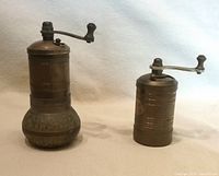 Both brass grinders side by side showing size difference and patina