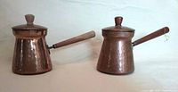 Both hammered copper pots with lids on, side view