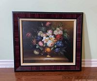 Full view of framed floral still life painting standing against wall