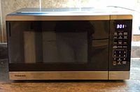 Front view of Toshiba countertop microwave showing brand badge, stainless trim, control panel and LED display