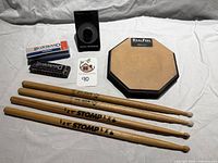 Group shot of drum pad, four drumsticks, metronome, harmonica with box