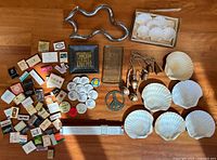 All items laid out showing slide rule, peace sign, square tray, sculpture, matchbooks, buttons, bells, shell plates, glass tray