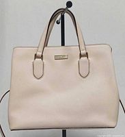 Front view of blush pink Kate Spade satchel showing logo plaque and top handles