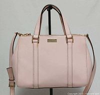 Front view of blush pink Kate Spade satchel showing logo plate, handles, strap