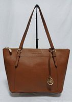Front view of brown Michael Kors saffiano leather tote with straps upright and MK charm