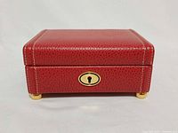 Front view of red leather jewelry box showing gold keyhole and feet