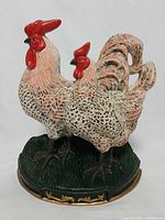 Front view of painted cast iron rooster and hen doorstop on green base