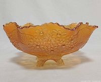 Side view of marigold carnival glass footed bowl showing Orange Tree pattern and ruffled rim