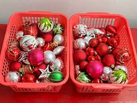 Two red plastic baskets filled with assorted red, silver and green ornaments