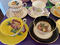 Group of assorted teacups and saucers showing yellow, black, cream and other floral designs
