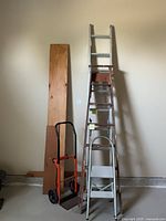 Group view of ladders, step stool, hand truck against wall