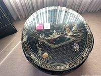Top view of round lacquer table showing inlaid scene and glass top