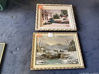 Both framed paintings side by side on floor, showing relative sizes and frames