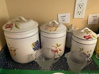 Front view of all four fruit-motif ceramic canisters with lids and two frosted cups