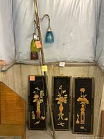 Tall metal floor lamp with two pendant glass shades and three lacquer floral panels displayed side by side