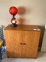 Wood cabinet with cranberry glass lamp on top
