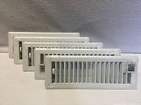 five shrink-wrapped white louvered floor registers lined up